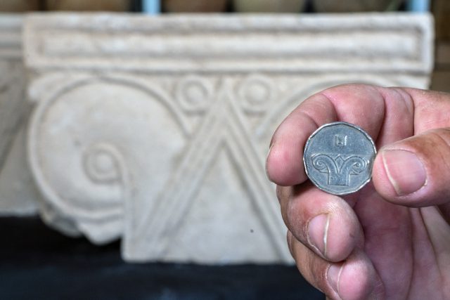 מטבע 5 שקלים על רקע הכותרת שנתגלתה.