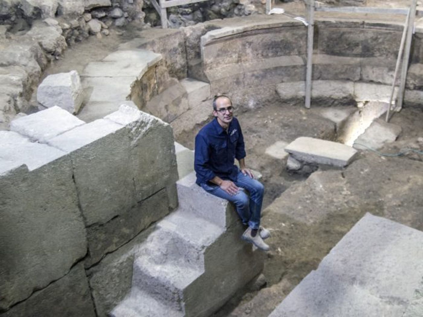 ד"ר ג'ו עוזיאל יושב על מדרגות מבנה התיאטרון (צילום באדיבות רשות העתיקות)