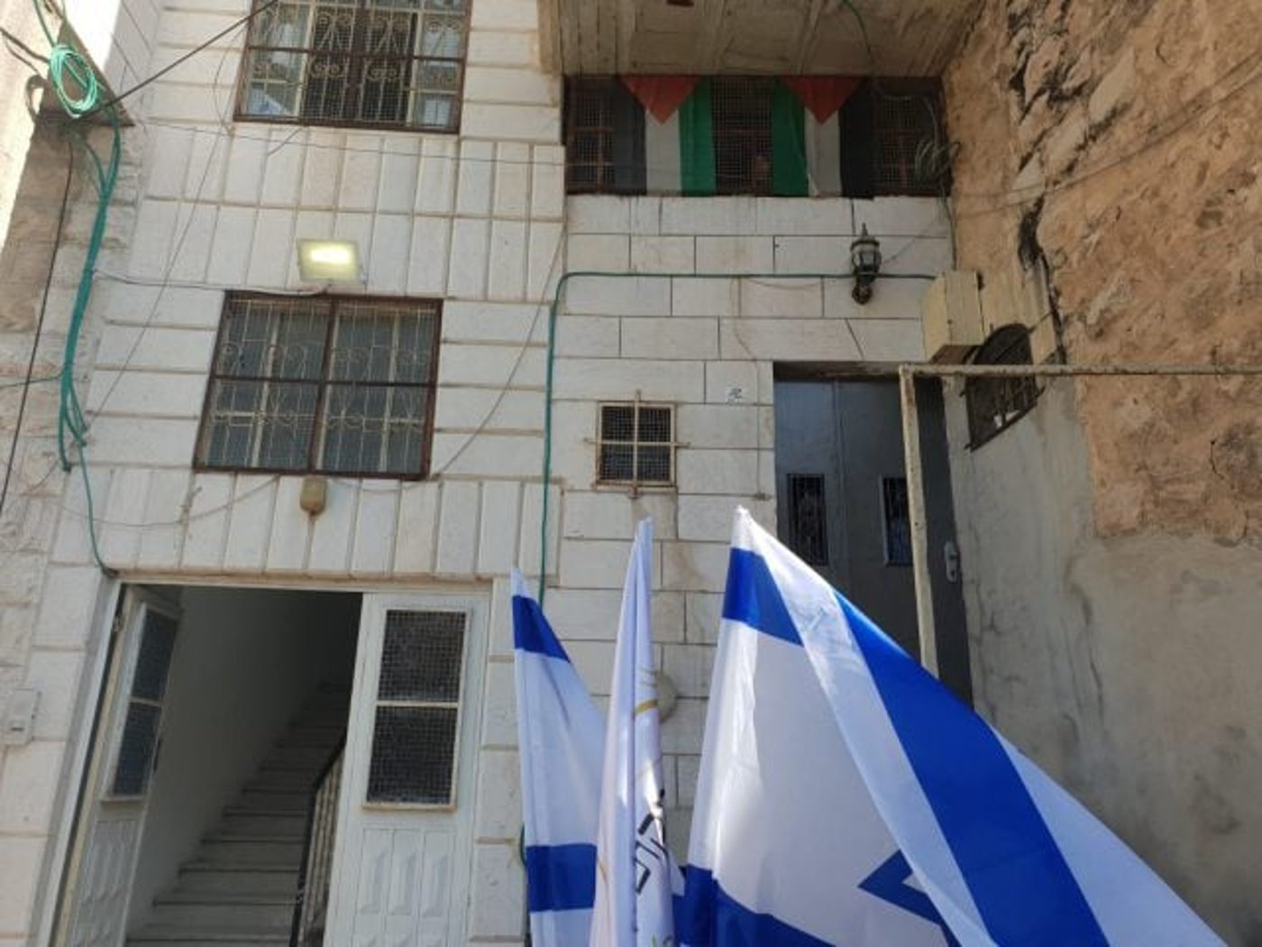 בית המכפלה. למטה דגלי ישראל, למעלה דגלי פלסטין. מימין הבית הפלסטיני, משמאל הבית היהודי.